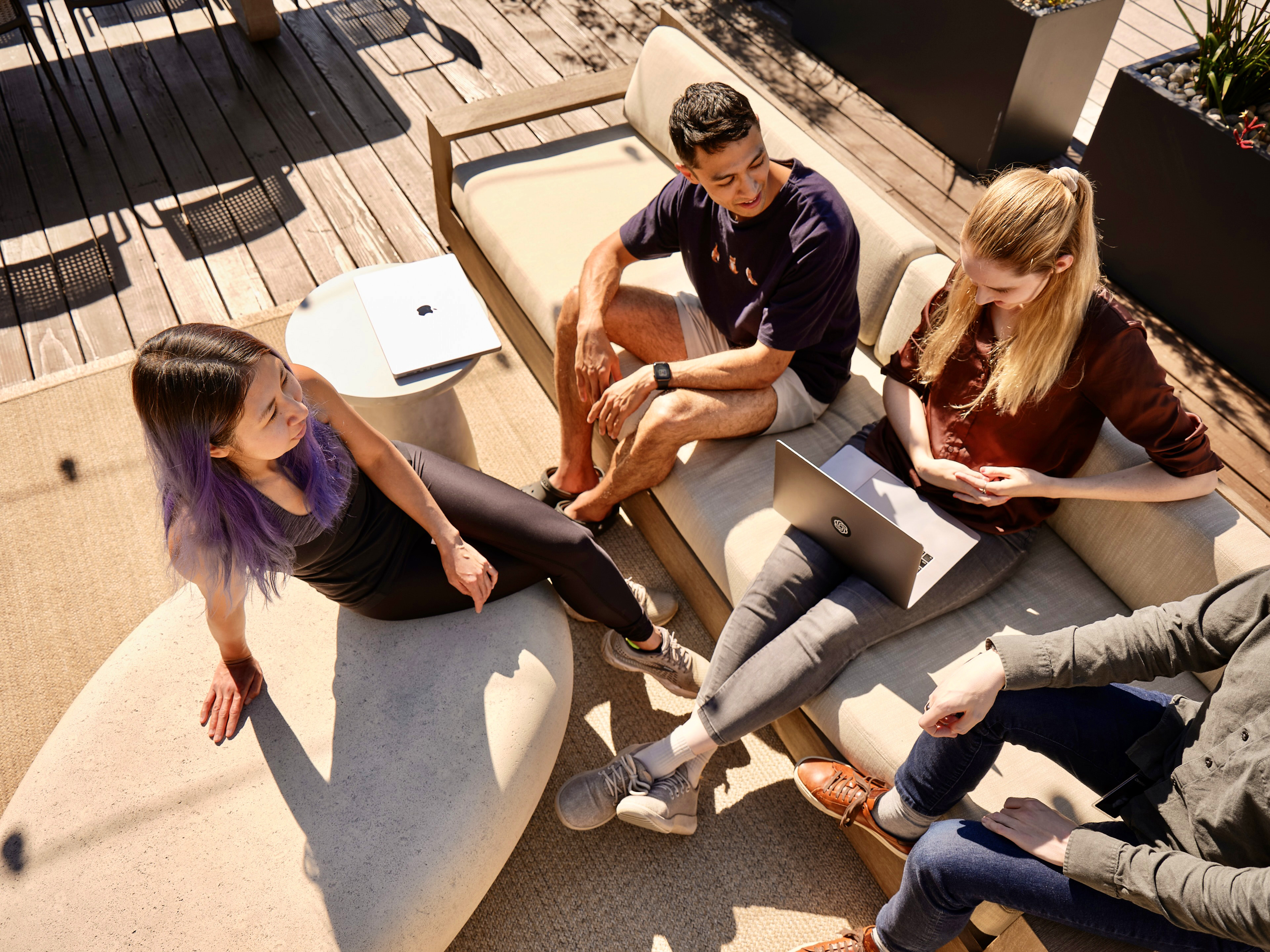 Four people lounging on a sunny roof deck, facing each other