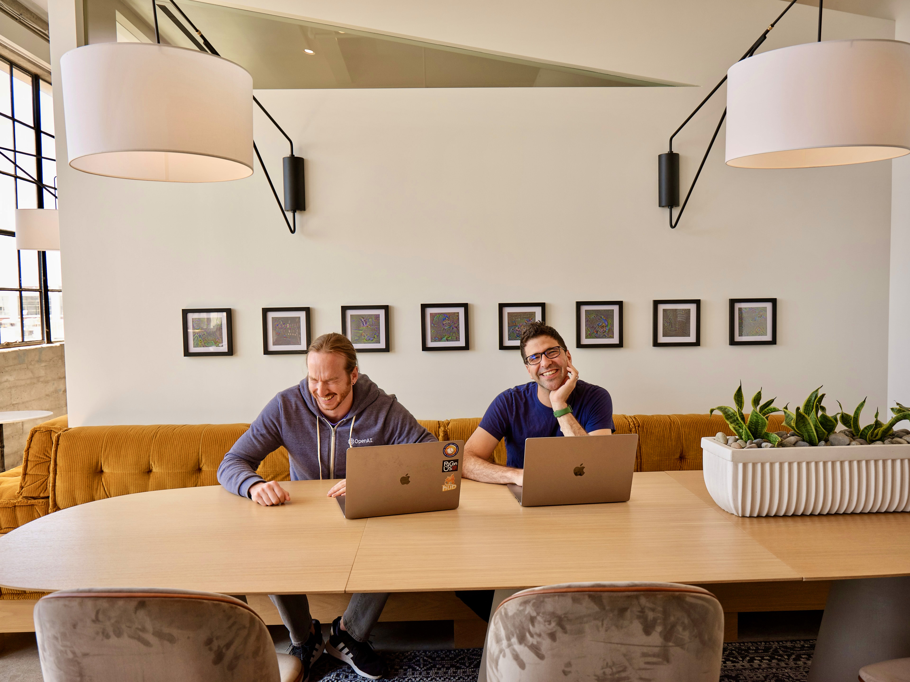 Two people laughing at a long table in front of their laptops